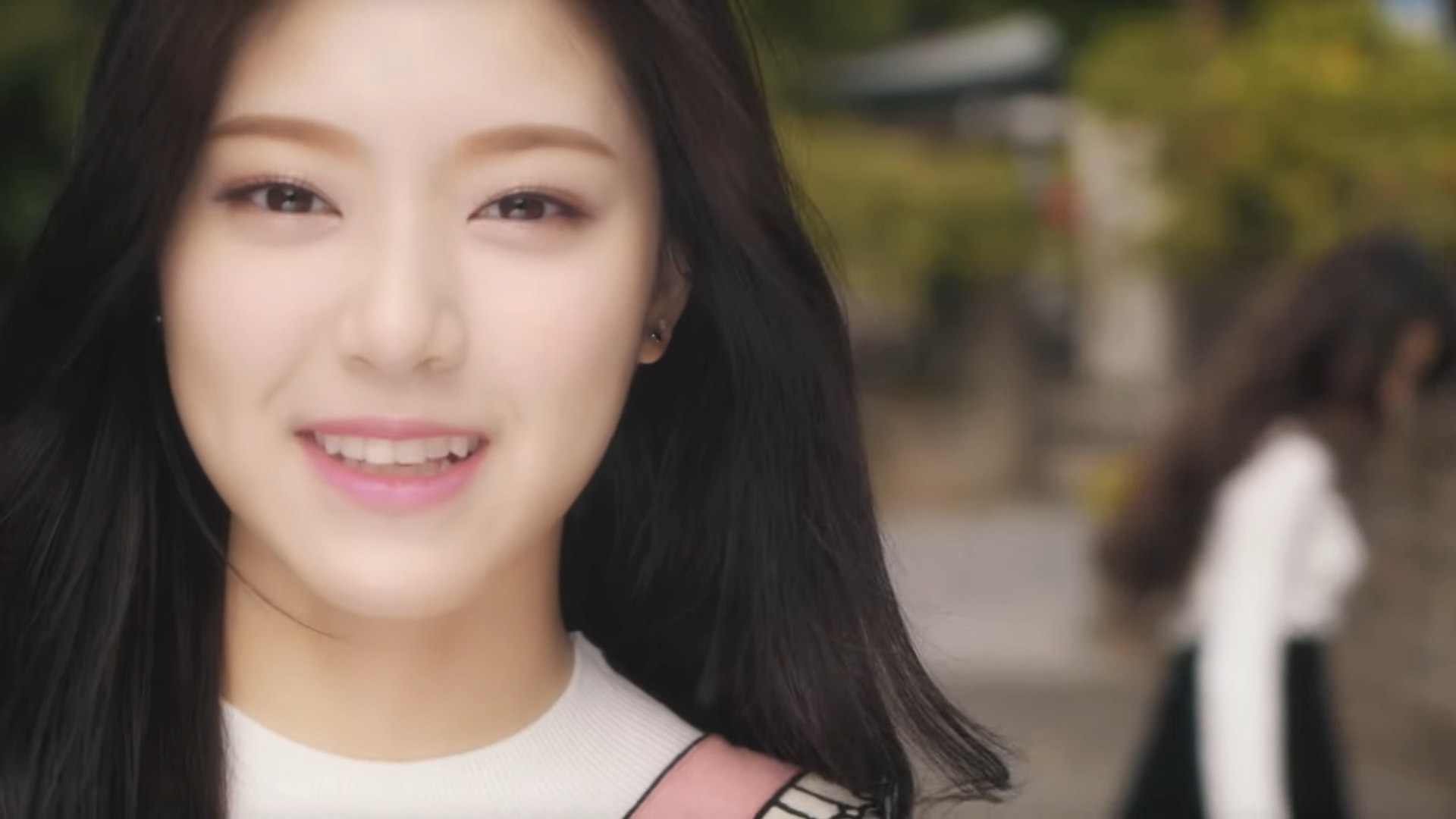 Hyunjin smiling at the camera. Heejin is standing in the background, blurred.
